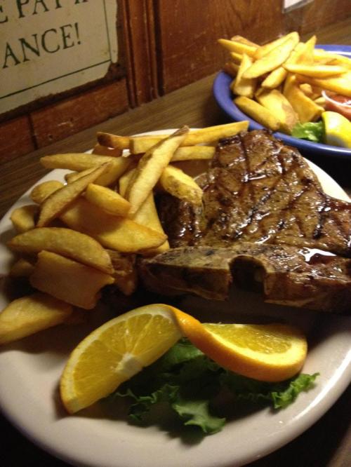 A plate of grilled steak with golden fries, garnished with a slice of orange and lettuce.
