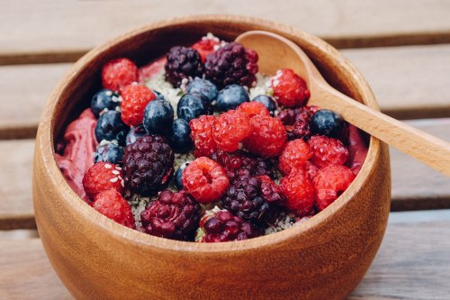 A wooden bowl filled with berry smoothie topped with raspberries, blueberries, and blackberries, garnished with seeds.