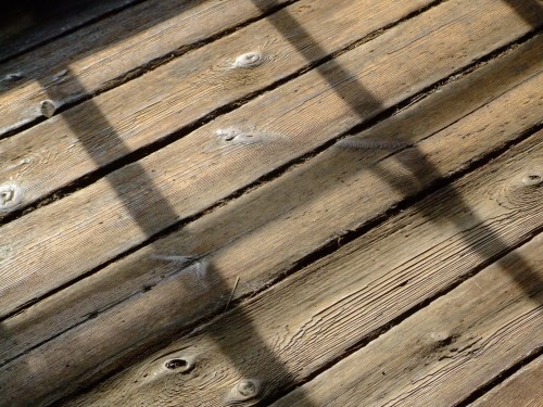 Sunlight casts shadows on weathered wooden floorboards, highlighting their texture and grain.