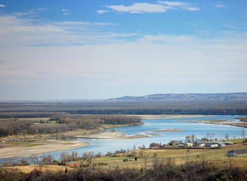 A serene river winding through a landscape of trees and hills under a clear blue sky.