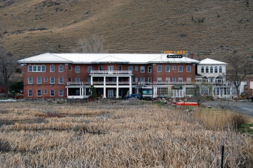 Historic Hot Lake Springs building surrounded by dry grass and hills, featuring a large sign and multiple balconies.