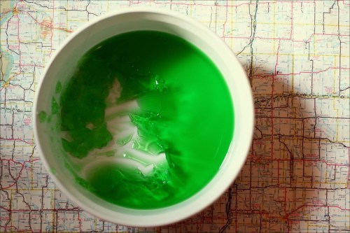 A white bowl filled with bright green gelatin sits on top of a colorful map.