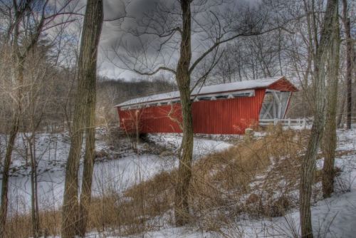 A red covered bridge surrounded by snow-covered trees and a frozen landscape.
