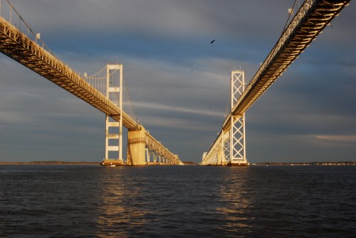 A view of two bridges spanning a river, with golden light reflecting on the water and a cloudy sky above.