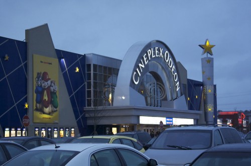 Cineplex Odeon movie theater exterior at dusk, featuring a large sign and a colorful star structure. Cars parked in front.