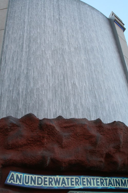 A large waterfall feature with a rocky base and a sign that reads "AN UNDERWATER ENTERTAINMENT."