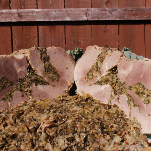 Sliced ham with a green herb filling, served alongside a mound of seasoned greens, against a wooden fence backdrop.