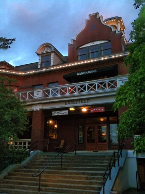Historic brick building with a decorative facade, featuring a sign for McMenamins Edgefield and stairs leading to the entrance.