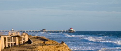 A scenic view of a pier extending into the ocean, with gentle waves and a clear blue sky.