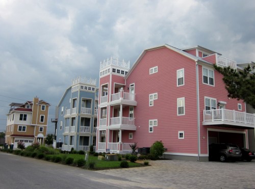 Colorful beach houses with balconies line a street under a cloudy sky.