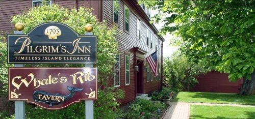 Sign for Pilgrim's Inn and Whale's Rib Tavern, featuring lush greenery and a classic red building with an American flag.