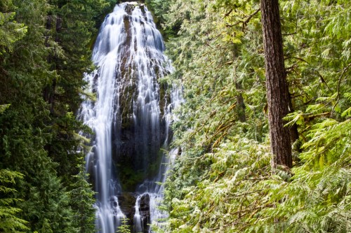 A majestic waterfall cascading down rocky cliffs, surrounded by lush green trees in a serene forest setting.