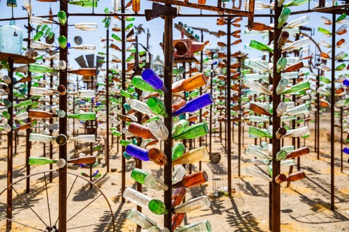 A colorful display of glass bottles arranged on metal structures in a sunny outdoor setting.