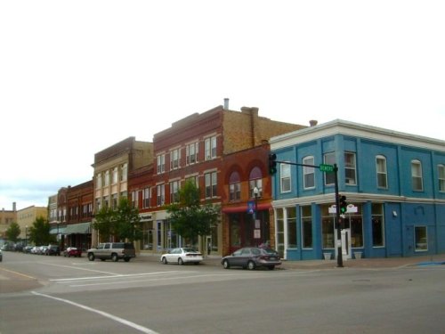 Historic buildings line a street, featuring red brick and blue facades, with trees and cars parked nearby.