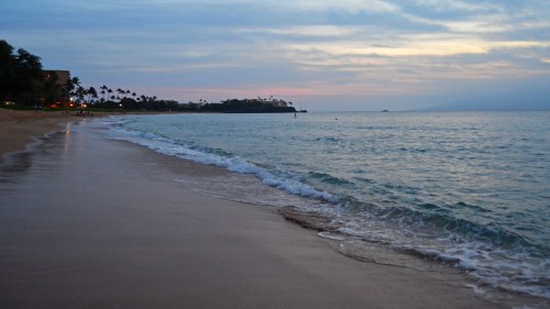 A serene beach at sunset, with gentle waves lapping at the shore and a cloudy sky in the background.