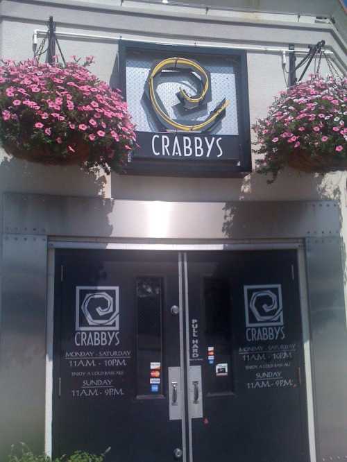 Exterior of Crabby's restaurant with hanging flower baskets and double doors displaying hours of operation.