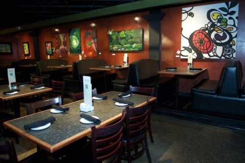 Interior of a restaurant featuring dark wooden tables, black chairs, and colorful artwork on the walls.