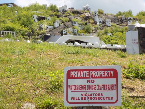 A red sign reading "Private Property" in front of a grassy hill with white structures in the background.