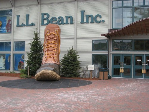 Giant boot sculpture at the entrance of L.L. Bean store, surrounded by trees and a brick walkway.