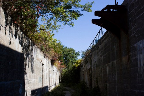 Abandoned concrete structure with overgrown vegetation and a clear blue sky above.