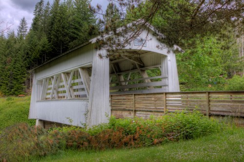 A white covered bridge surrounded by lush greenery and trees in a serene outdoor setting.