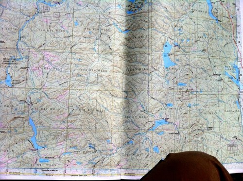 A detailed topographic map showing mountains, lakes, and rivers, with a person's leg visible at the bottom.