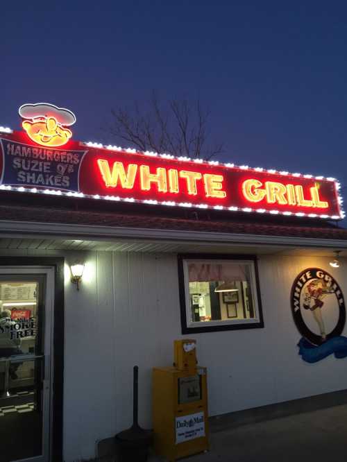 Neon sign for "White Grill" restaurant, featuring burgers and shakes, illuminated at dusk.