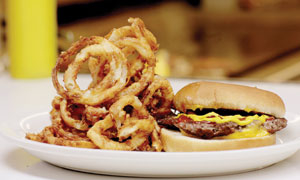 A plate with a cheeseburger topped with mustard and a large serving of crispy onion rings.