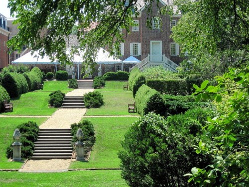 A well-maintained garden with neatly trimmed hedges, steps leading to a brick building, and a tent in the background.