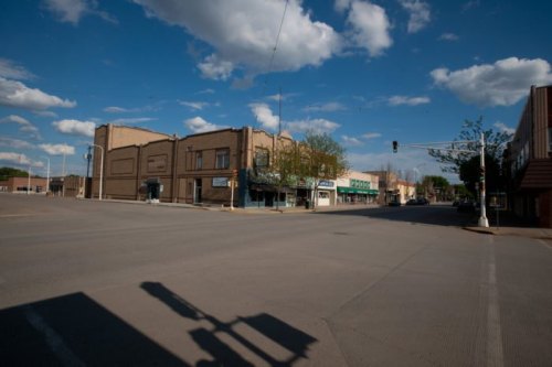 A quiet street scene featuring buildings, traffic lights, and a blue sky with scattered clouds.
