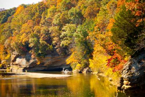 A serene river scene surrounded by vibrant autumn foliage and rocky cliffs reflecting in the water.