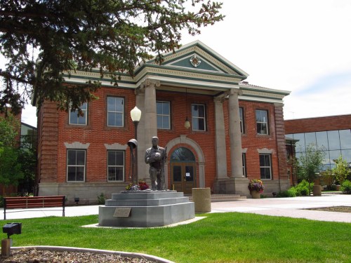 Historic brick building with columns, a statue in front, and landscaped green space.