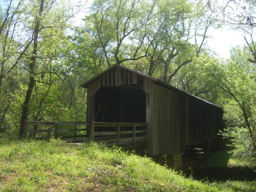 A rustic covered bridge surrounded by lush green trees and foliage on a sunny day.