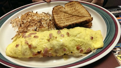 A plate with a ham and cheese omelet, golden hash browns, and two slices of toasted bread.