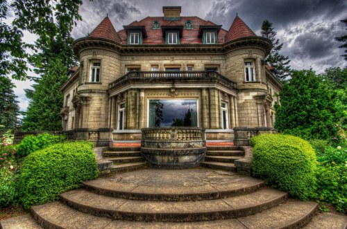 A grand, historic mansion with ornate architecture, surrounded by lush greenery and a dramatic cloudy sky.