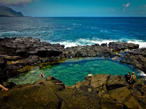 A natural pool surrounded by rocky shores, with people swimming and enjoying the ocean view under a clear blue sky.