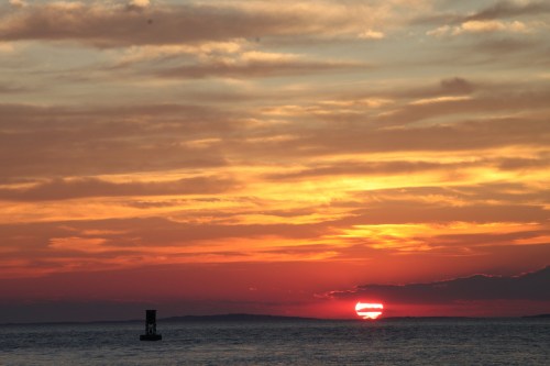 A vibrant sunset over the ocean, with colorful clouds and a silhouette of a buoy in the foreground.