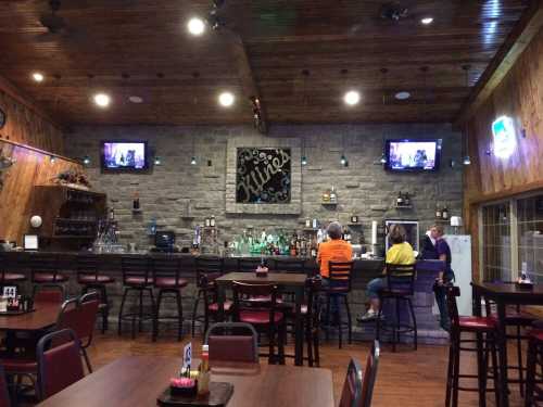 Interior of a rustic bar with stone walls, a well-stocked bar, and patrons seated at tables and the bar.