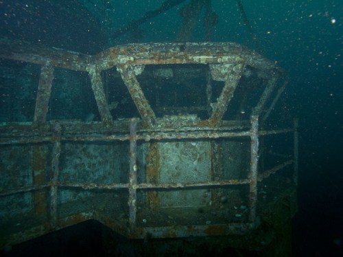 Underwater view of a rusted, submerged structure with a grid-like design, surrounded by murky water.