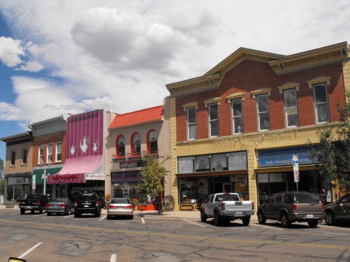 A charming street scene featuring colorful storefronts and parked cars under a partly cloudy sky.