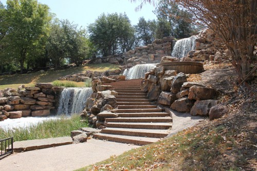 A serene landscape featuring cascading waterfalls, stone steps, and lush greenery in a park setting.