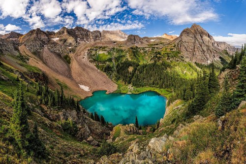 A stunning mountain landscape featuring a turquoise lake surrounded by lush greenery and rocky peaks under a blue sky.