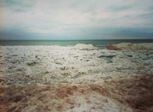 A cloudy sky over a frozen shoreline with ice and snow covering the ground and floating on the water.