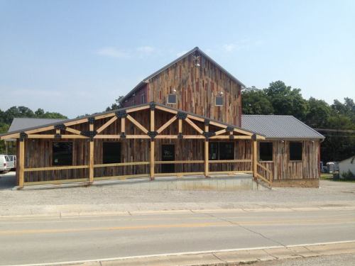A rustic wooden building with a sloped roof and large front porch, set against a clear blue sky.