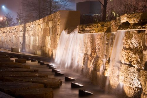 A serene water feature with cascading waterfalls and illuminated stones, set in a misty, nighttime environment.