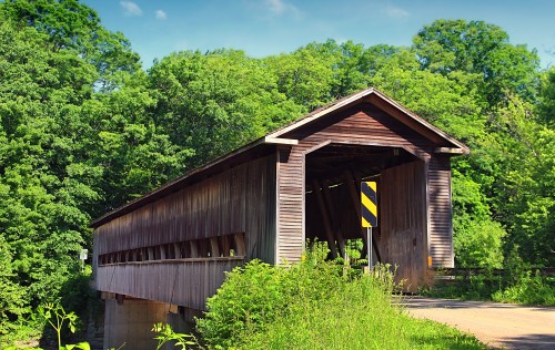 A wooden covered bridge surrounded by lush green trees under a clear blue sky.