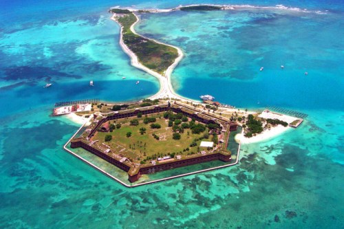 Aerial view of a coastal fort surrounded by turquoise waters and a sandy path leading to a small island.