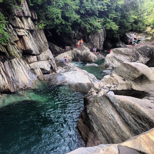 A scenic river with clear water surrounded by rocky cliffs and people enjoying the natural landscape.