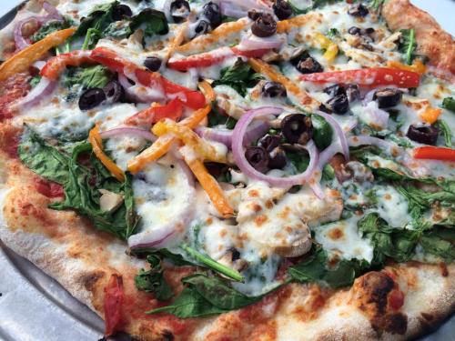 A close-up of a veggie pizza topped with spinach, bell peppers, onions, olives, and melted cheese on a crispy crust.