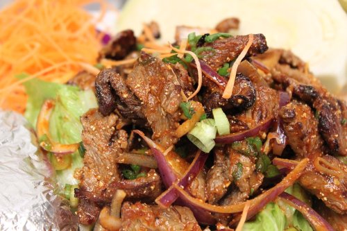 A close-up of a flavorful beef dish topped with vegetables, served on a bed of lettuce and garnished with herbs.